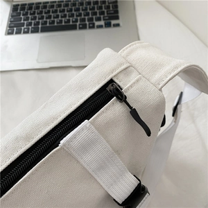 Detailed close-up of high-quality zipper and stitching on a white canvas messenger bag