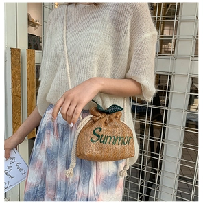 Detail of straw bucket bag with green leaf accents and Summer embroidery on a model