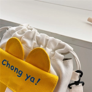 Detail of canvas drawstring bucket bag featuring a yellow ear flap and blue text