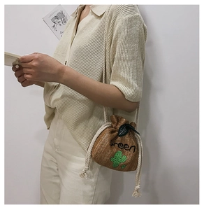 Detail of straw bucket bag featuring green embroidery and cactus patch with drawstring