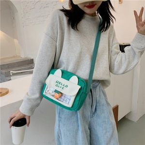 Detail of green canvas crossbody bag with white rabbit ear flap and Hello Girl text