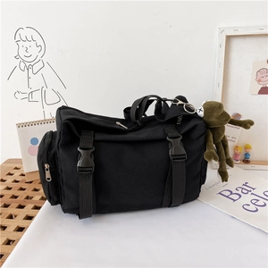 Dettaglio della borsa a tracolla in tela nera con fibbie funzionali e ciondolo in peluche verde