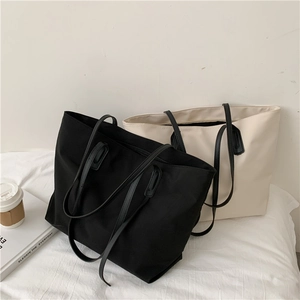 Large tote bags in black and beige displayed on a bed with a coffee cup and books