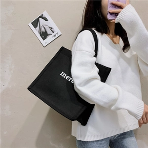 Side view of a large black canvas tote bag with white lettering worn by a model