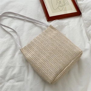 Straw shoulder bag with white lace trim and straps on a minimalist fabric background
