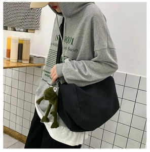 Borsa a tracolla in tela nera capiente con ciondolo a forma di rana verde indossata