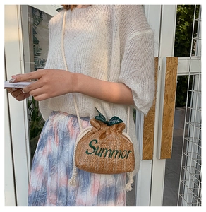 Detail of handwoven straw bucket bag with green leaf accents and Summer embroidery