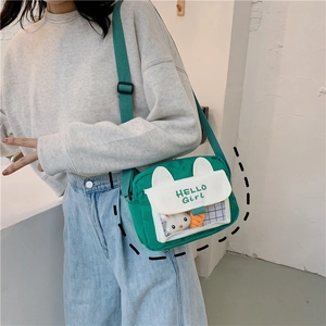 Detail view of green canvas crossbody bag featuring cute white rabbit ears and clear window