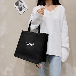 Detail of black canvas tote bag with white merci print on a female model