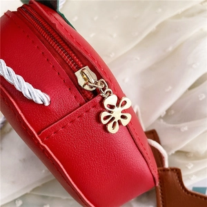 Macro detail of red strawberry bag showing gold flower zipper and leather texture
