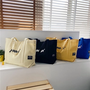 Close-up of four canvas tote bags in white, black, yellow, and blue with geometric logos