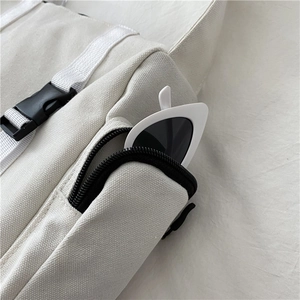 Detail of white canvas bag showing zipper pocket, wide strap and adjustable buckle