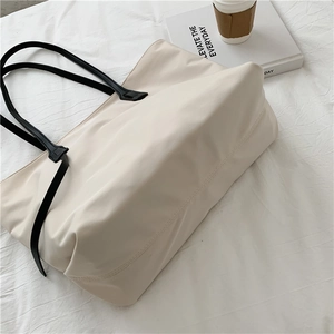 Detailed macro view of cream nylon tote bag with black handles and aesthetic props