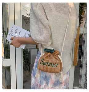 Detail of straw bucket bag featuring green Summer embroidery and leaf accents