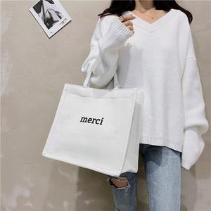 Close-up of white canvas tote bag with black merci print and canvas handles