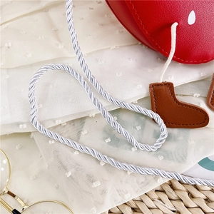 Close-up of red strawberry crossbody bag with rope strap and boot charms for girls