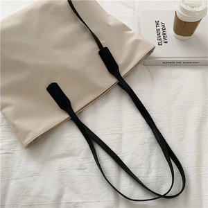 Detail shot of a minimalist cream tote bag with black straps on a textured fabric