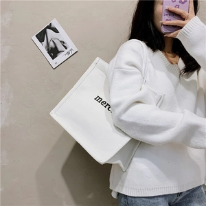 Detailed shot of white canvas tote bag with black merci print and sturdy straps