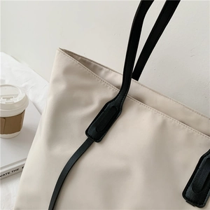 Detail of off-white waterproof tote bag showing black leather handle and reinforced stitching