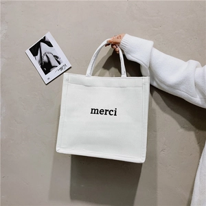 Detail of minimalist white canvas tote bag featuring black merci lettering print