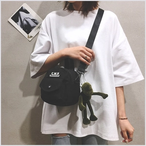 Détail d'un sac bandoulière en toile noire avec lettres blanches et charm grenouille