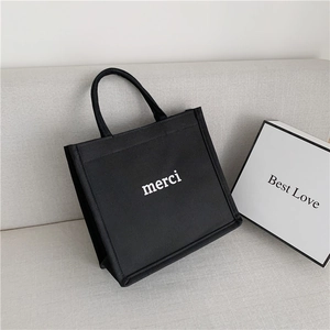 Close-up of black canvas tote bag with white merci print on a minimalist sofa