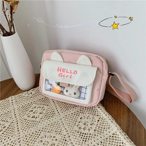 Detail of canvas crossbody bag showing Hello Girl print and plush rabbit charm decor