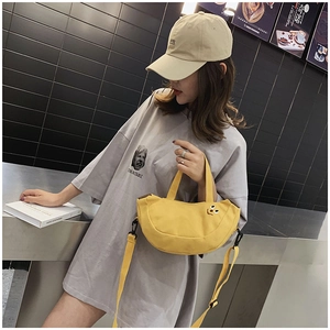 Détail d'un sac bandoulière en toile jaune avec broderie sourire porté par un mannequin