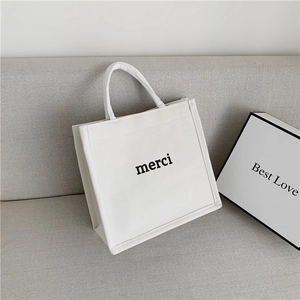 Detail of white canvas tote bag with black merci print on a soft grey sofa