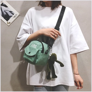 Détail du sac bandoulière en toile vert menthe avec logo CMN et peluche de grenouille