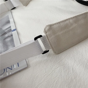 Detailed macro view of white canvas bag shoulder strap with black adjustable buckle