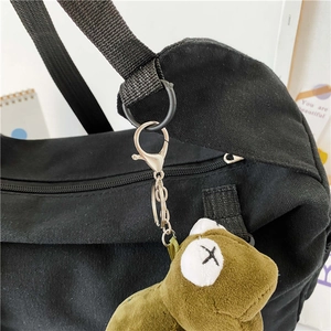Dettaglio del ciondolo peluche verde con occhi a X sulla borsa in tela nera