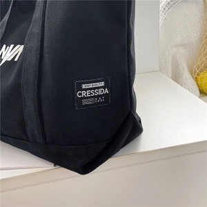 Detail shot of the durable black canvas tote bag showing stitching and retro brand label