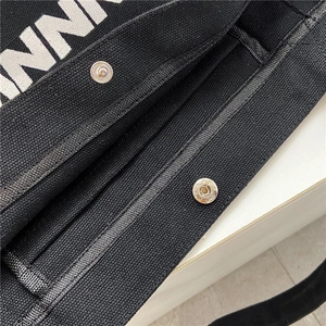 Detail of black canvas tote bag with metal snap button and reinforced webbing