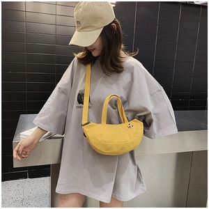 Détail du sac demi-lune en toile jaune avec broderie porté par un mannequin