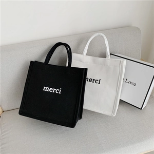 Detailed view of canvas tote bags with 'merci' print in black and white colors