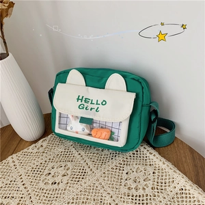 Detail view of canvas crossbody bag with cat ears and rabbit charms on a lace table