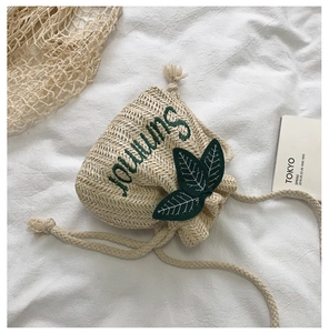 Detail of beige straw bucket bag with green leaf accents and embroidery on fabric