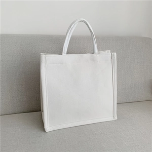 Detail of white canvas tote bag showing stitching quality on a light gray fabric surface