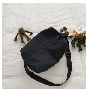 Dettaglio di una borsa a cilindro in tela nera con zip superiore e tracolla larga