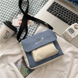 Flat lay of blue and beige canvas messenger bag with planet embroidery and accessories