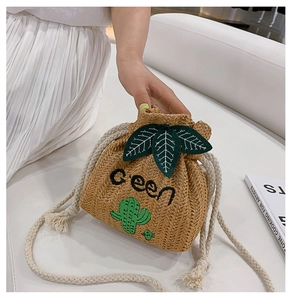 Detail of straw bucket bag featuring green cactus embroidery and leaf-shaped drawstring closure