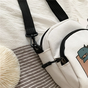 Détail du sac bandoulière en toile blanche avec imprimé dinosaure et sangle en nylon
