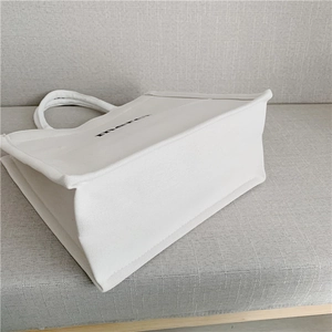 Detailed close-up of white canvas tote bag side profile with black merci printing
