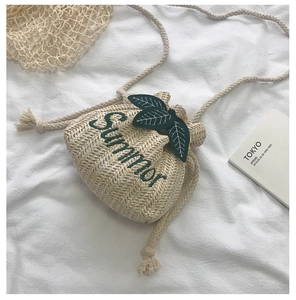 Detail of straw bucket bag with green Summer embroidery and decorative leaf charm
