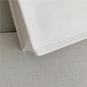 Detailed close-up of stitching and weave texture on white canvas tote bag corner