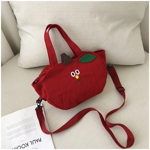 Détail du sac bandoulière en toile rouge en forme de pomme avec décor de feuilles