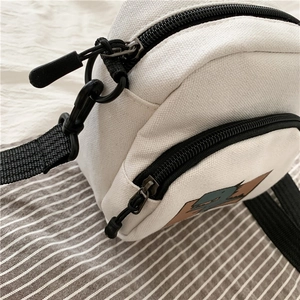 Détail du sac bandoulière en toile blanche avec motif dinosaure mignon et zips noirs