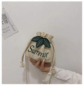 Detail of beige straw bucket bag with green leaf embroidery and cotton rope strap