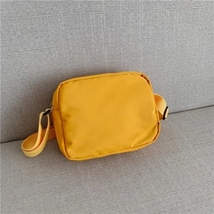 Close-up of bright yellow canvas crossbody bag with adjustable strap on grey fabric